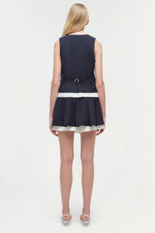 Navy pleated skort with white stripe trim, belted waist, sleeveless design, worn with clear heels.