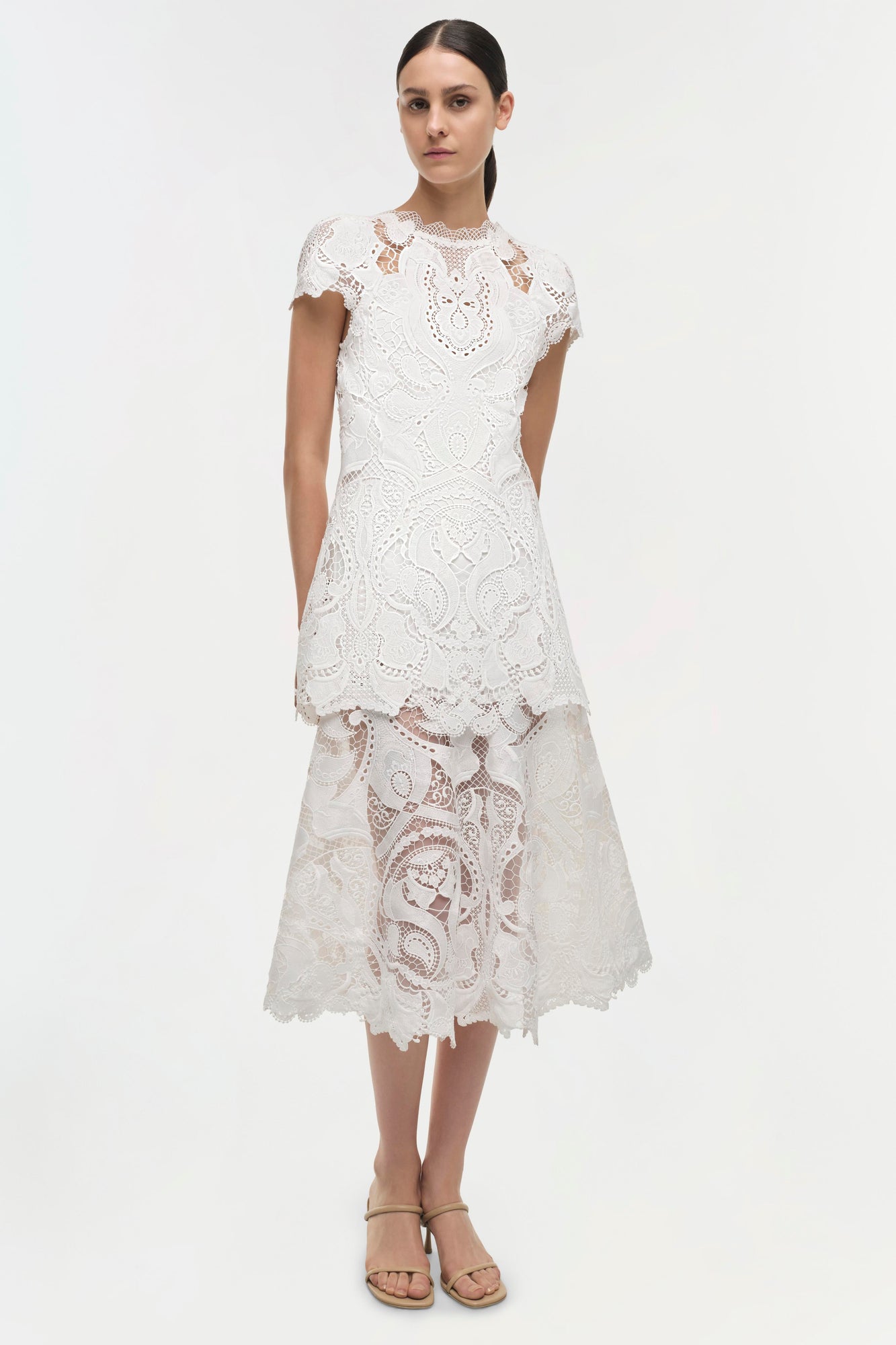 White lace dress with short sleeves, decorative cutout patterns, and asymmetrical tiered skirt.