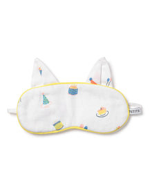 The Kids Twill Kitty Sleep Mask in Birthday Wishes by Petite Plume is a luxurious white eye mask with yellow trim, featuring colorful cake, party hat, and balloon illustrations. It includes two fabric ears, an elastic strap, and can be monogrammed for personalization.