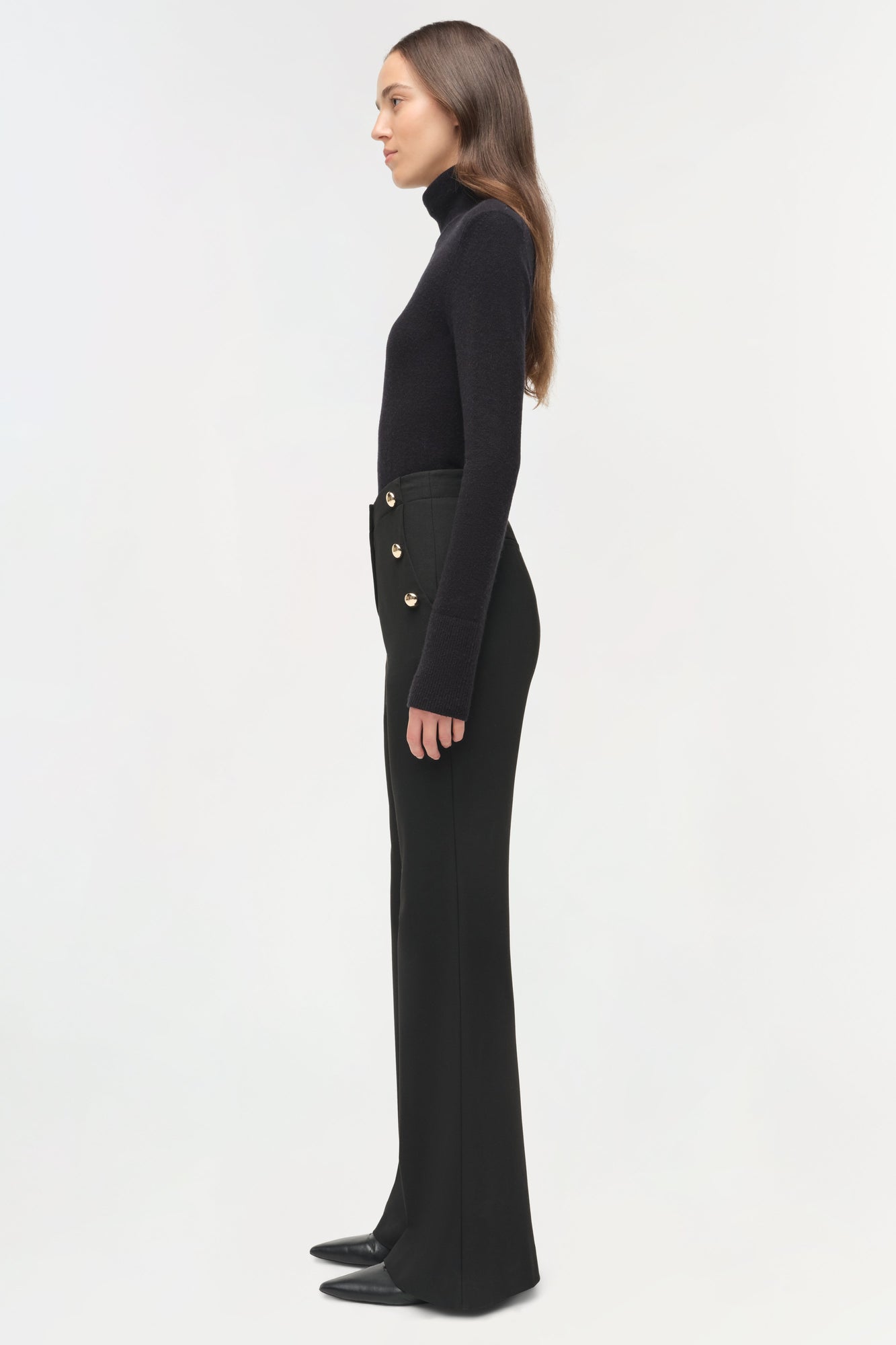 Black tailored trouser with gold button details at waist, worn with black turtleneck, side view on model.
