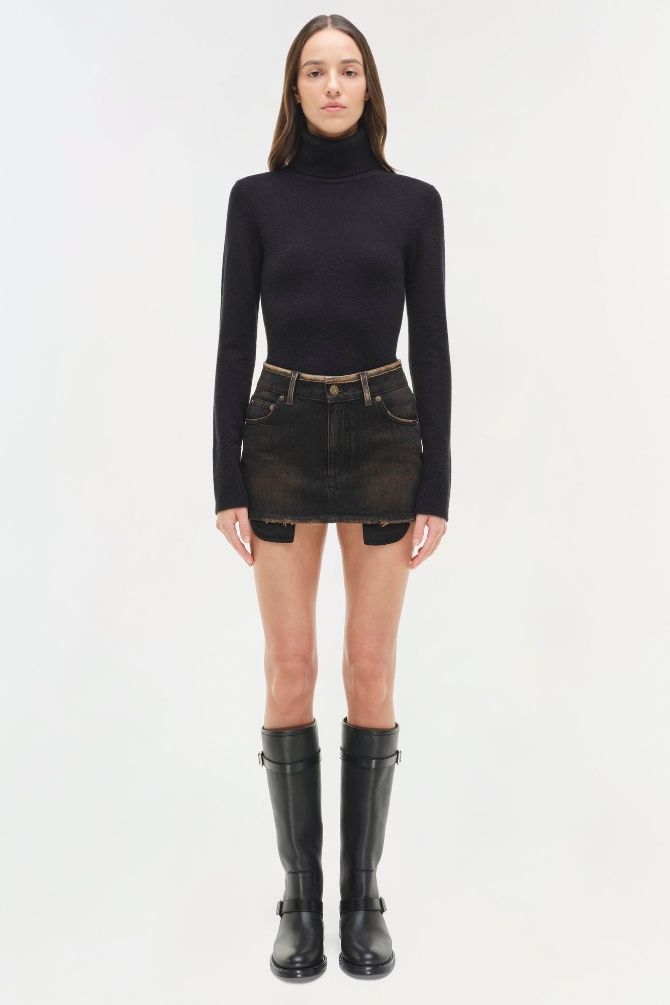 Black denim mini skirt with distressed details and button waistband, styled with black turtleneck and boots.