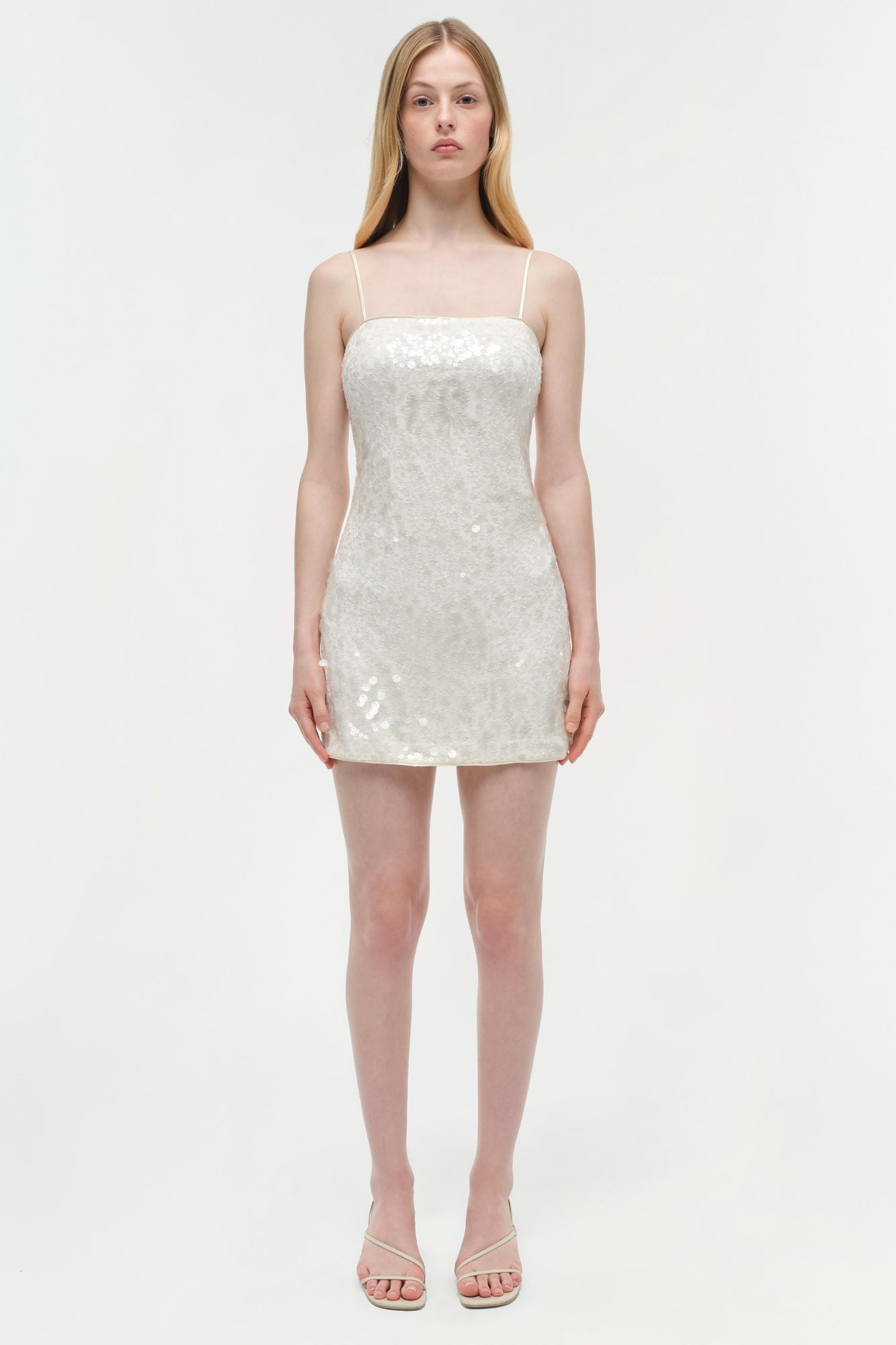 White sequined mini dress with thin straps on model wearing nude sandals.