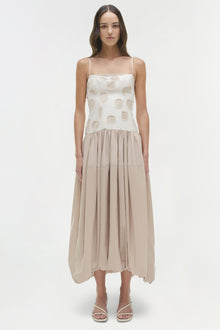 Woman wearing a cream and beige midi dress with geometric circle print top and pleated skirt, paired with white sandals.
