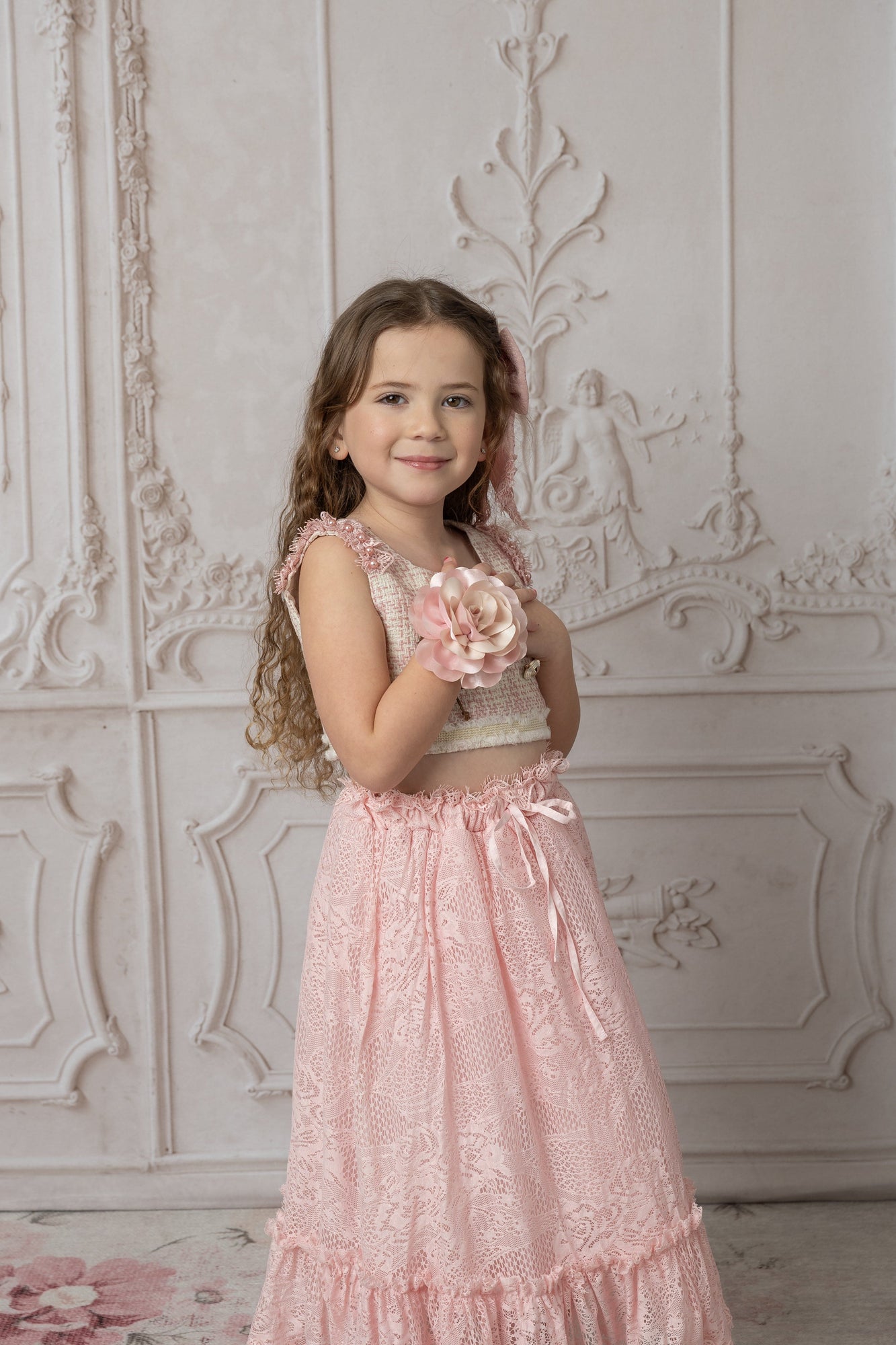 Girl wearing a beige and pink tweed top with a floral bracelet and pink lace skirt 