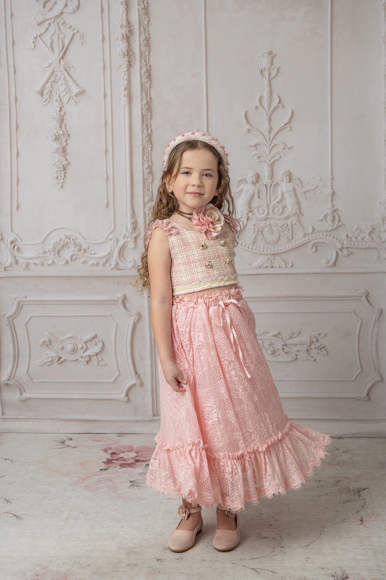Girl wearing a beige and pink tweed top with a floral necklace and pink lace skirt, along with a matching tweed headband