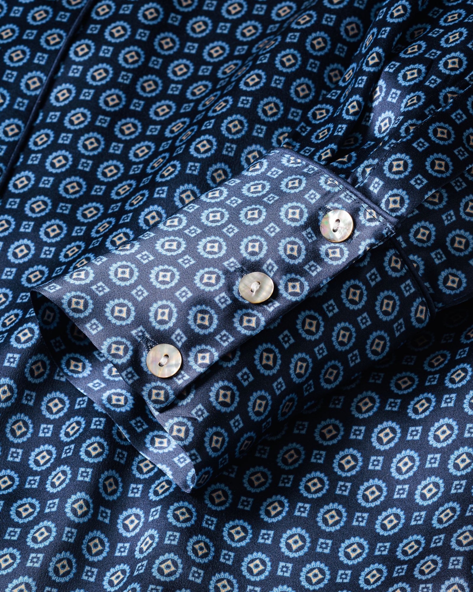 Close-up of a Womens Silk Nightshirt in Midnight Foulard by Petite Plume, showcasing its blue geometric pattern, alternating light and dark tones. The cuff features three light-colored buttons.