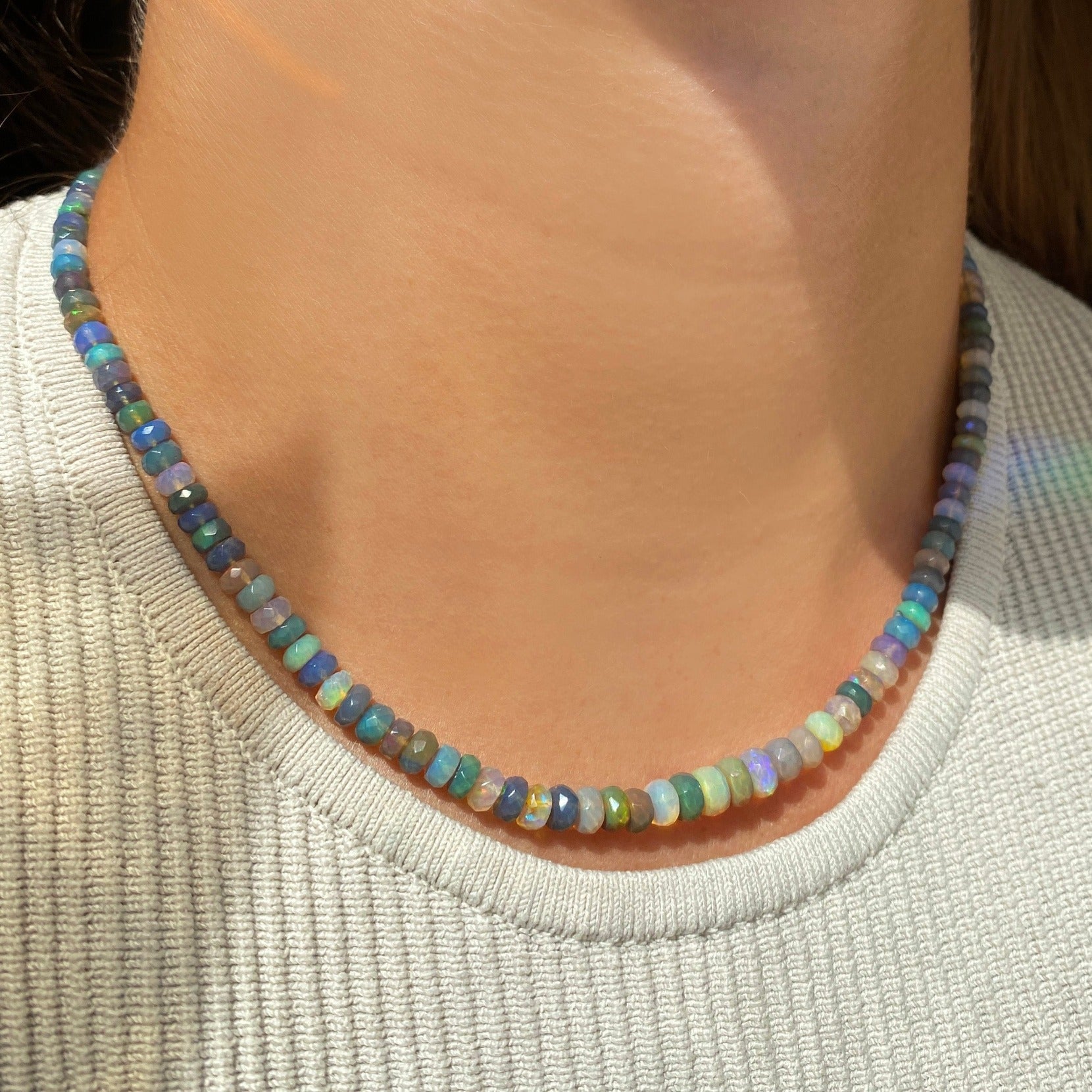 Shimmering beaded necklace made of faceted opals in shades of light blue, light purple, yellow, white, and clear on a gold linking ovals clasp.