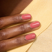 A close-up of a hand with short, neatly manicured nails painted in Manucurist's glossy Bois de Rose shade, resting on yellow knit fabric.