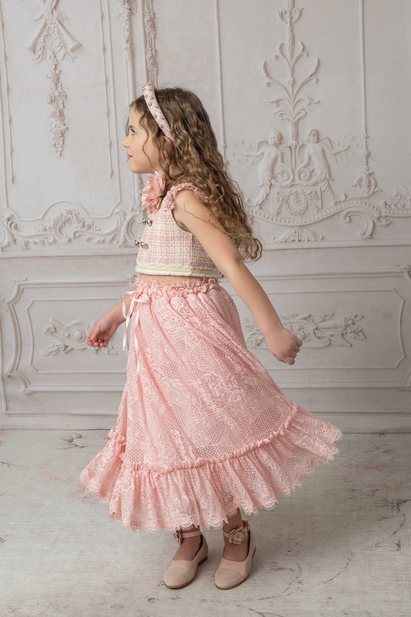 A girl wearing a pink and beige tweed top with a pink ruffle lace skirt
