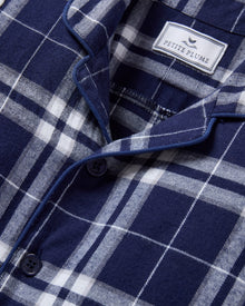 The Baby's Brushed Twill Classic Romper in Oxford Tartan is a full-length, long-sleeve children's onesie featuring a navy, white, and gray plaid pattern with a button-up front, collar, and snap leg closures.
