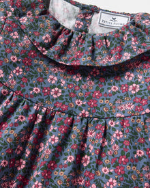The Girl's Twill Scarlett Nightgown in Fleurs de Saison is a long-sleeved, knee-length dress with a ruffled collar and cuffs, featuring pink and white flowers with green leaves on a dark background.