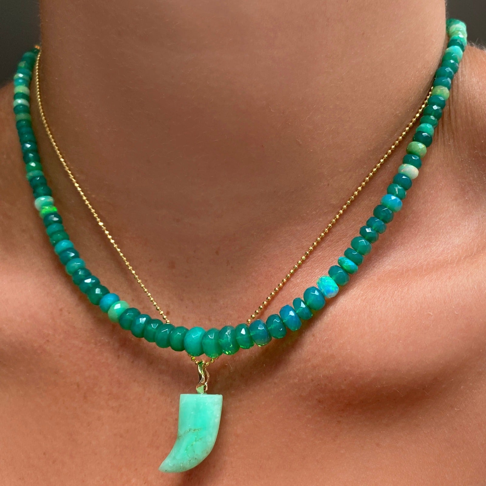 Shimmering beaded necklace made of faceted opals in shades of green on a gold linking ovals clasp. Styled on a neck layered with the diamond cut bead chain necklace and horn charm.