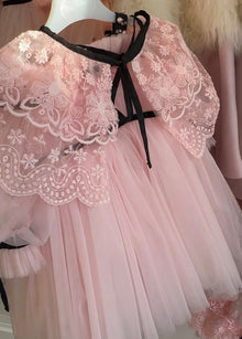 Close up of blush pink lace cape accessory with a black waist bow detail, highlighting the texture and pattern of the lace