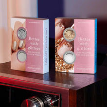 Two pink and white boxes of Manucurist Glitters Duo Silver  Mirror sit side by side on a dark surface, each featuring nail designs with silver glitter, mirror effect powder, rose gold, and glazed shades.
