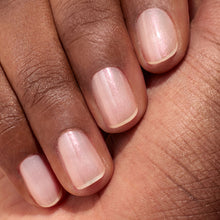 A close-up of a hand with medium brown skin, showcasing neatly manicured nails painted in Manucurist's Glitters Duo Rose Gold  Glazed—a sheer pale pink polish with a delicate pearlescent shine.