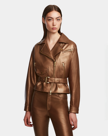 A woman wearing the Rudsak ARIELLE - 8124052 Antique Bronze shiny brown lamb leather jacket with gold zippers and matching brown leather pants, standing against a plain white background.