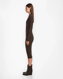 A woman in profile stands against a white background, wearing a fitted womens bodycon dress and Rudsak AGNES - 8524551 Espresso dark brown ankle boots with buckles. Her straight hair is worn down.