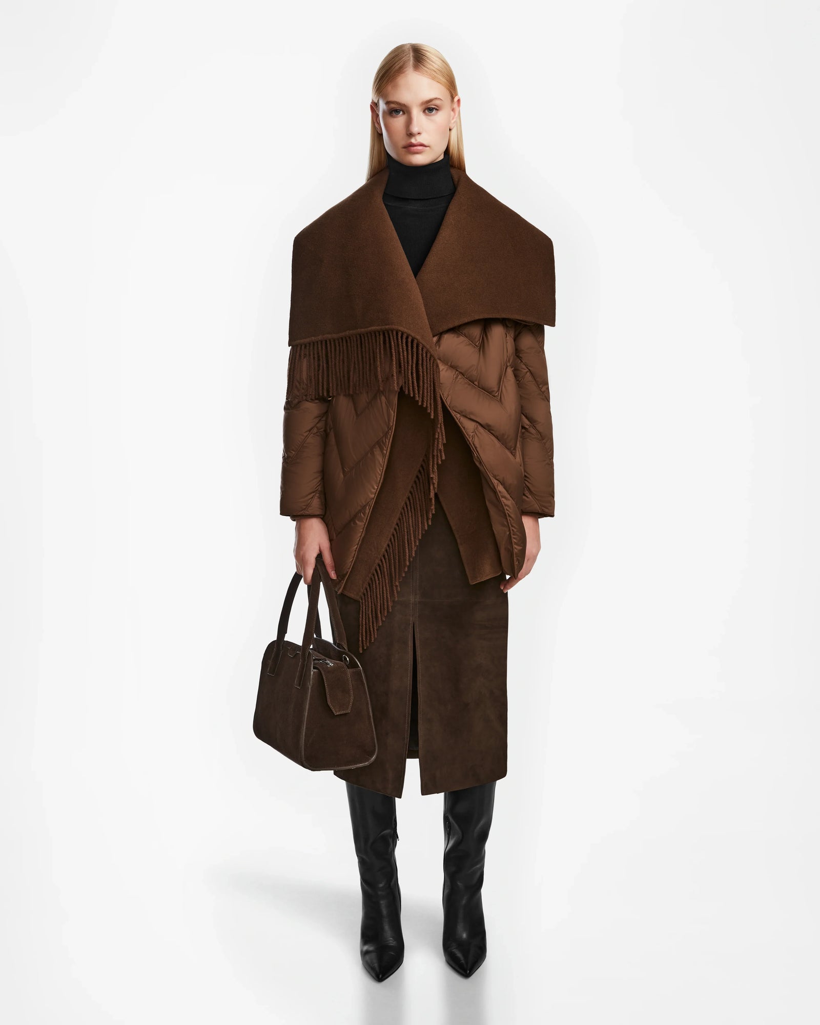 A woman poses against a plain backdrop wearing the Rudsak ANNE MARIE - 8124713 Mocha coat with fringe accents, styled with a black turtleneck, brown skirt, black knee-high boots, and a brown handbag.