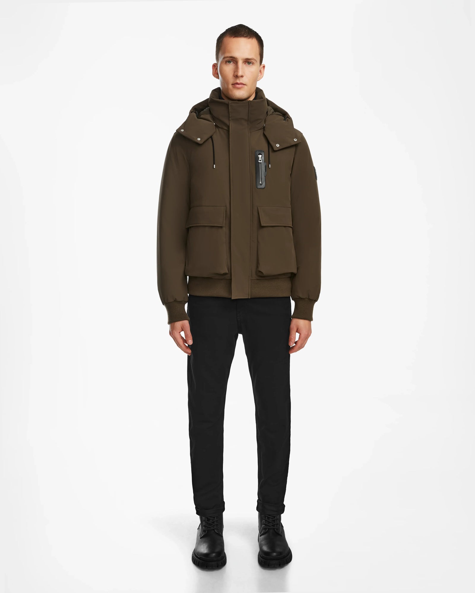 A person stands facing forward in an urban style, wearing the Rudsak ASH - 6124599 Army mens down bomber jacket with large front pockets, black pants, and black shoes against a plain white background.