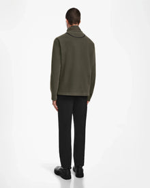 A man, facing away from the camera against a white background, wears the Rudsak BECK - 6524538 Army jacket with vegan leather trims, paired with black pants and black shoes.