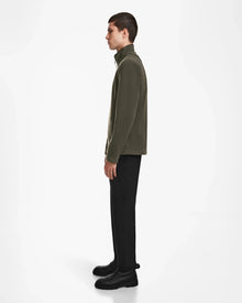A person stands in profile against a white background, wearing the Rudsak BECK - 6524538 Army half-zip pullover featuring vegan leather trims, paired with black pants and shoes.