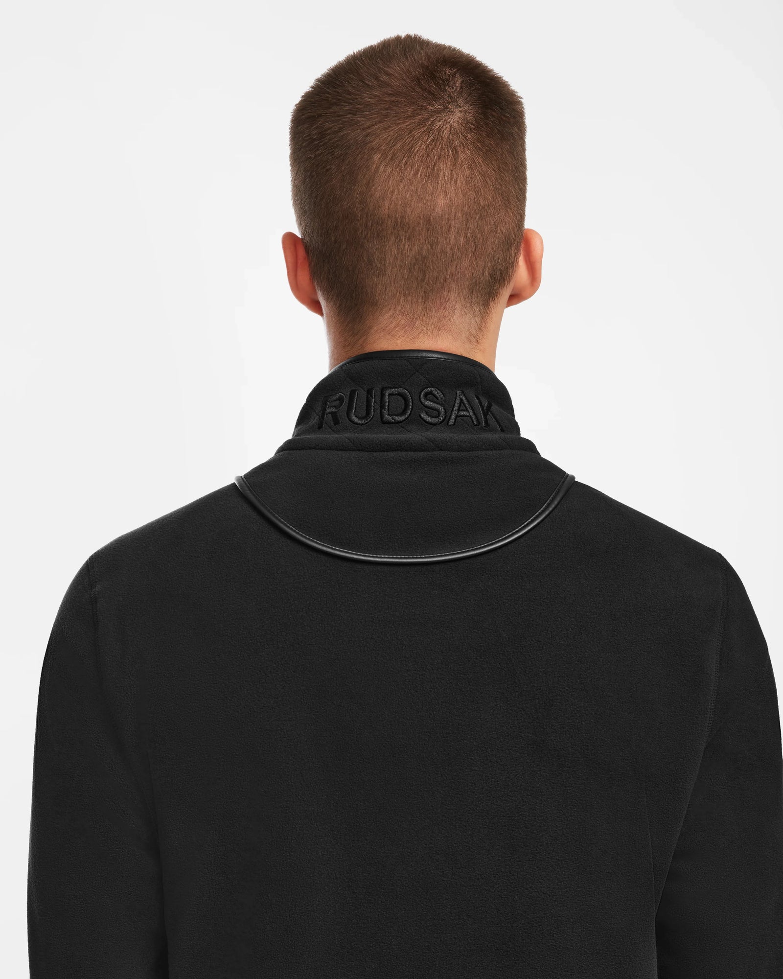 A person with short brown hair is shown from behind in the Rudsak BECK - 6524538 Black jacket, featuring a raised RUDSAK collar and subtle vegan leather trims—perfect for casual style. The background is plain white.