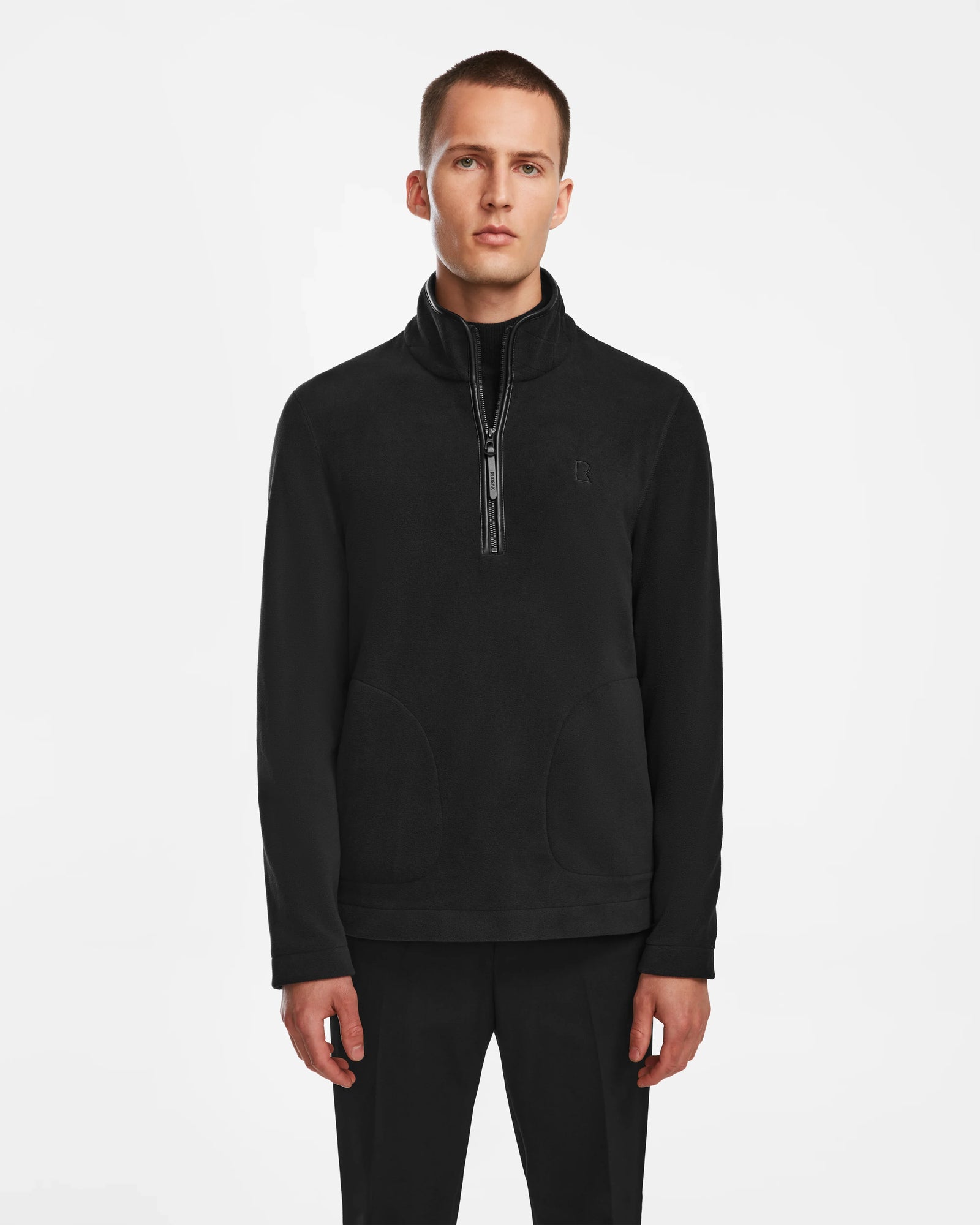 A man with short hair and a neutral expression models the Rudsak BECK - 6524538 Black men’s fleece half-zip pullover with front pockets and vegan leather trims, set against a plain white background, ideal for casual wear.
