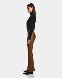 A woman stands in profile against a plain background, wearing a black long-sleeve turtleneck top paired with Rudsak’s CARISSA - 8524545 Antique Bronze leather pants and black boots.