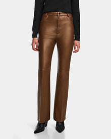 A person wears Rudsak’s CARISSA - 8524545 Antique Bronze high-waisted leather pants with a slight flare, black pointed-toe shoes, and a long-sleeve black top, standing against a plain white background.