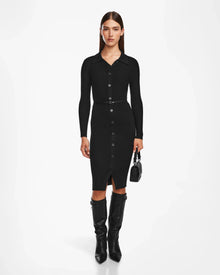 A woman faces forward wearing the Rudsak CARLI - 8524573 Black fitted, long-sleeve, collared knit dress with a vegan leather belt, styled with knee-high black boots and a small black handbag against a plain white background.
