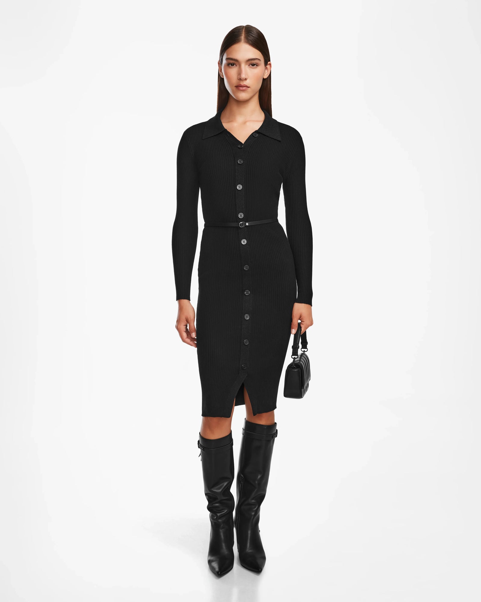 A woman faces forward wearing the Rudsak CARLI - 8524573 Black fitted, long-sleeve, collared knit dress with a vegan leather belt, styled with knee-high black boots and a small black handbag against a plain white background.
