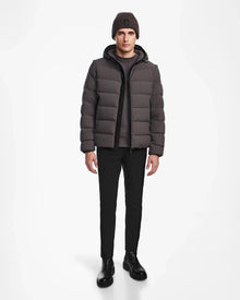 A man faces forward with a neutral expression, wearing the Rudsak DEMIAN M-R - M123504 Grey mens down puffer jacket, paired with dark pants, black boots, a gray knit beanie, and a gray shirt against a white background.