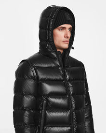 A man in the Rudsak DEMIAN S-R - M123505 Black down puffer jacket with hood up and a black knit beanie, glancing to the side against a plain white background.