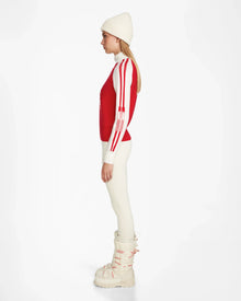 Woman in profile wearing the Rudsak FANNY - 8524506 Flame Red après-ski sweater, a white beanie, cream leggings, and white boots, posed against a plain white background.