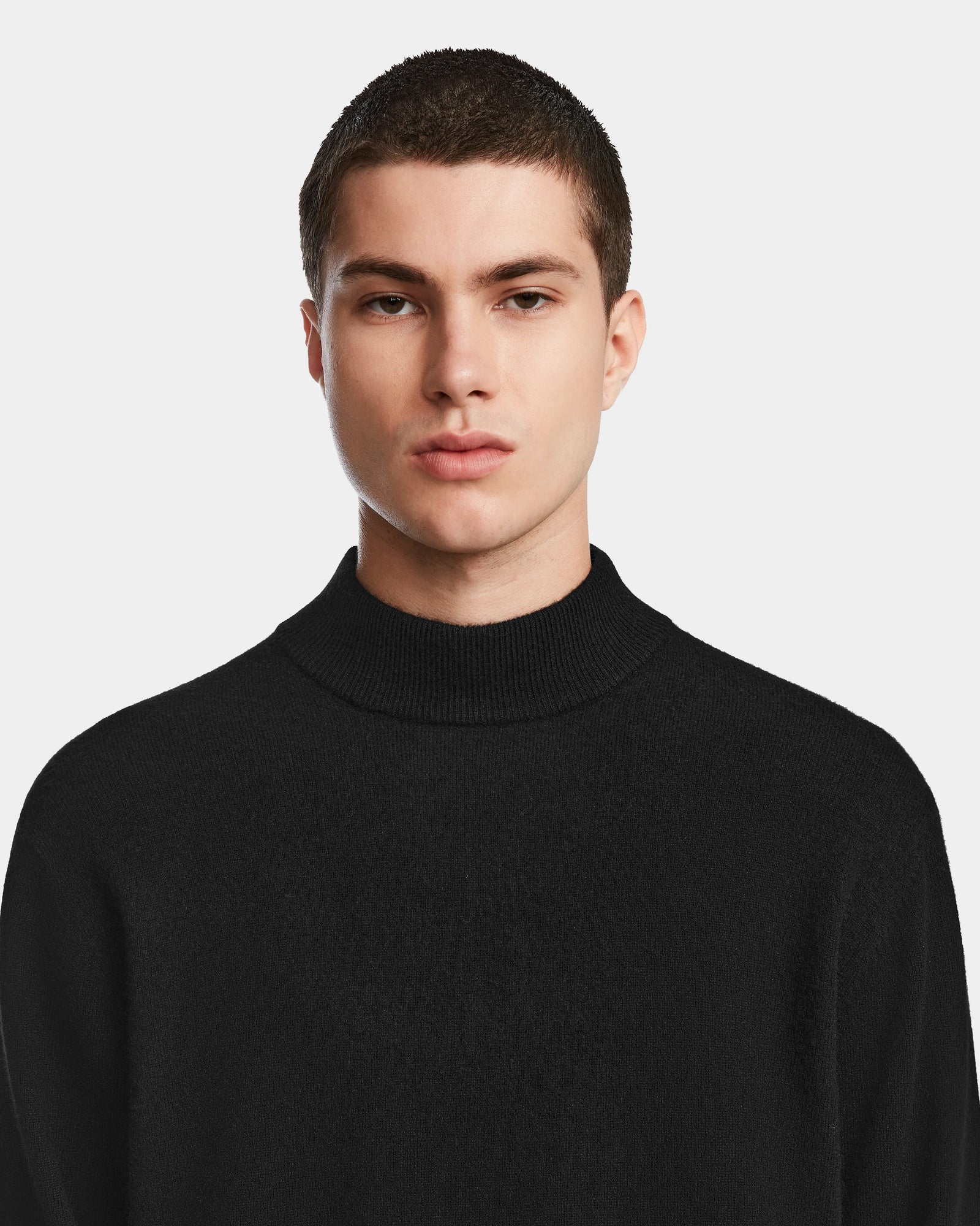 A young man with short dark hair wears the Rudsak FERRAN - 6524511 Black mens turtleneck sweater, looking directly at the camera against a plain light background.