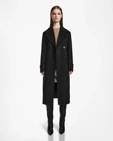 A woman faces forward wearing the IVE - L124560 Black womens wool blend long coat by Rudsak, paired with a brown top, gray skirt, and black knee-high boots against a plain white background.