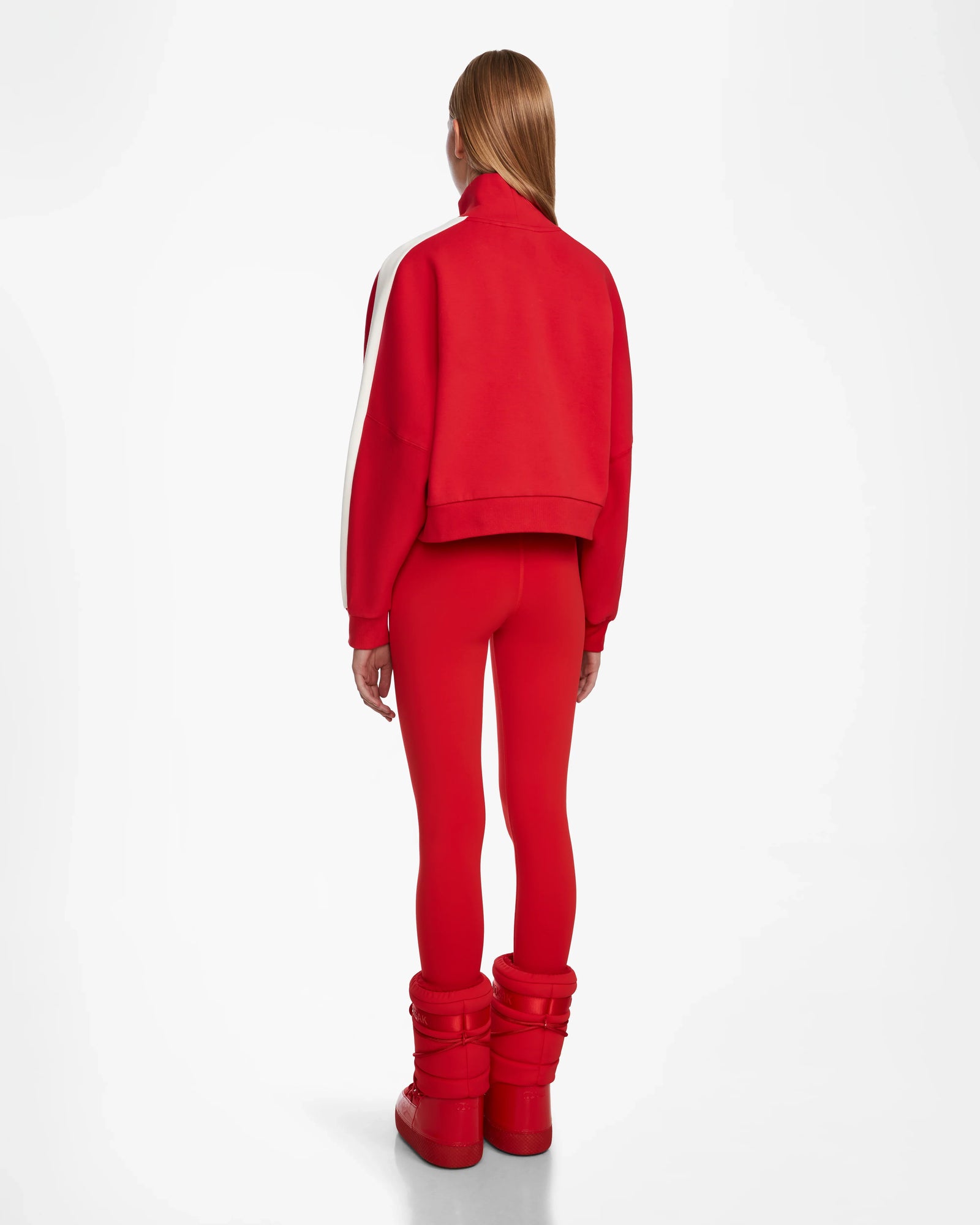 A person with straight, long hair stands facing away, modeling the Rudsak KELLIE - 8524615 Flame Red set: a relaxed fit top with white sleeve detail, matching leggings, and padded boots, all against a plain white background.