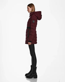 A woman in profile wears the Rudsak MALAYA M - L123554 Wine down puffer jacket with a hood, black belt, black leggings, and black ankle boots against a white background.