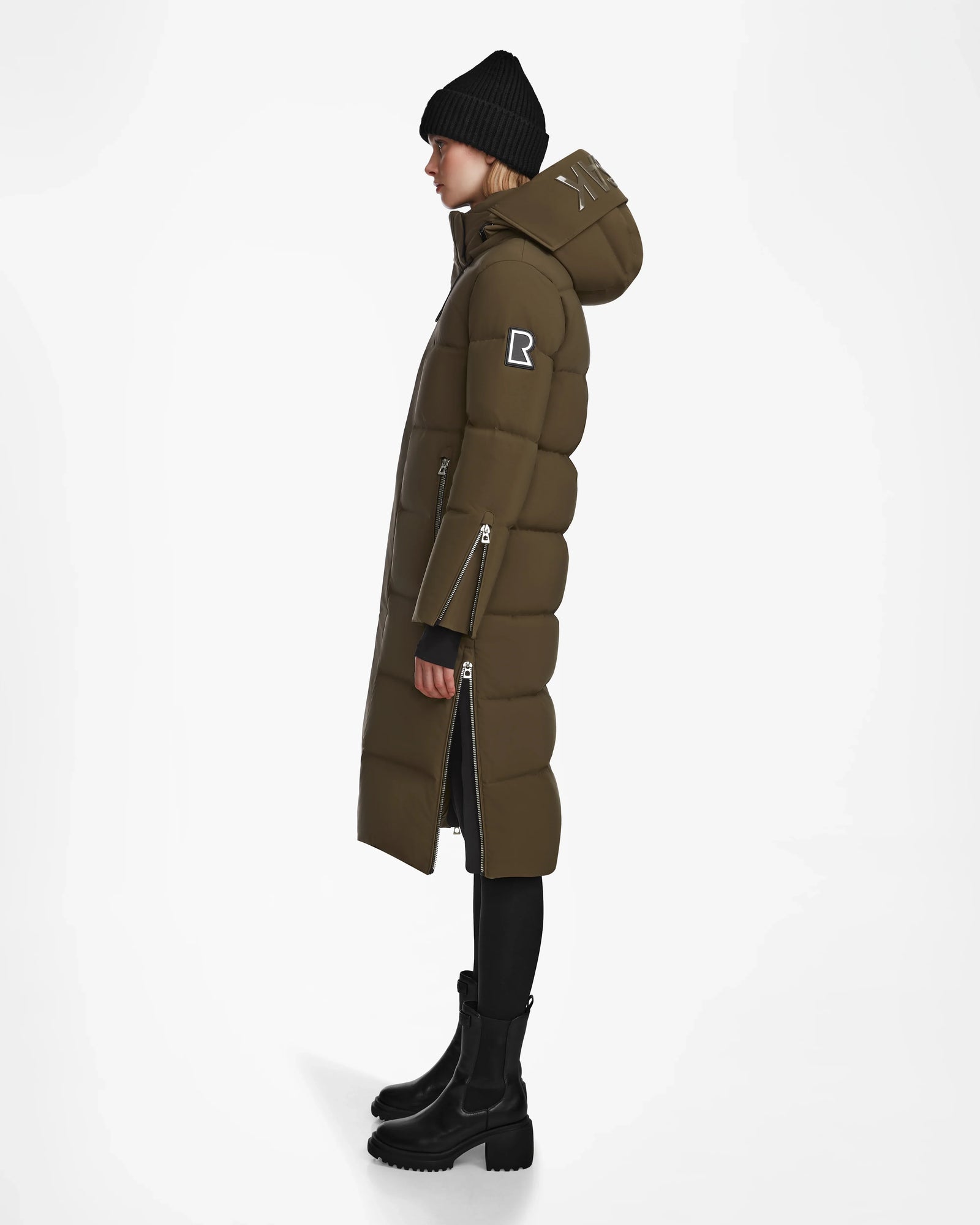 A person in profile wears the Rudsak MAO M - 8123598 Army women’s down puffer coat, made from weatherproof recycled Stormshell, styled with a black beanie, black pants, and chunky boots against a plain white background.