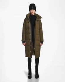 A person stands facing forward wearing the Rudsak MAO M - 8123598 Army long olive green womens down puffer coat, made from weatherproof recycled Stormshell, paired with a black beanie, sweater, pants, and boots against a white background.