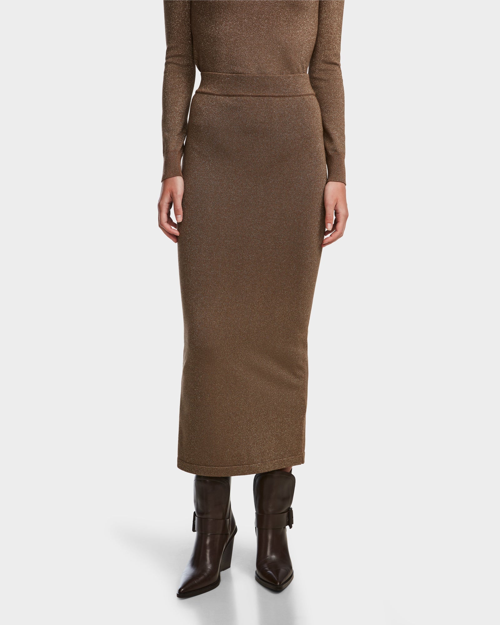 A person wears the MONICA - 8524516 Antique Bronze fitted women’s knit skirt by Rudsak, styled with a matching brown top and dark brown heeled boots, against a white background. Upper body partially visible.