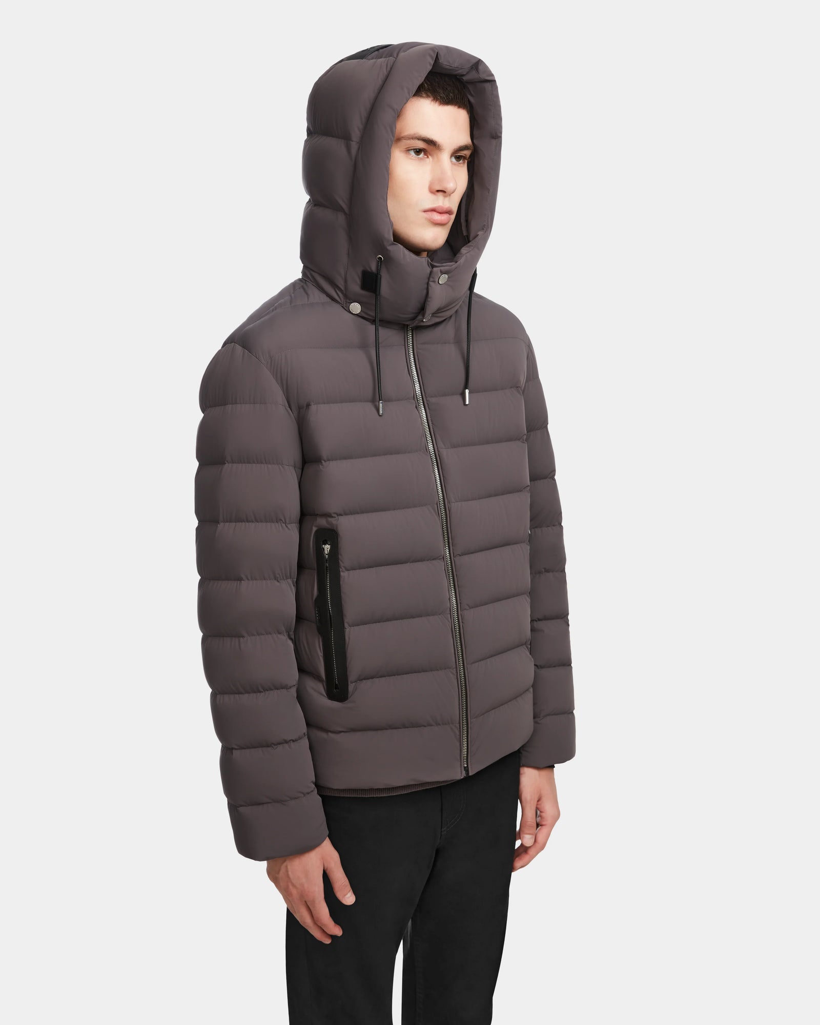 A person wears the Rudsak NAVAN - 6124551 Grey men’s quilted down puffer—an RDS-certified, hooded, zippered jacket thats wind and water-repellent—standing against a plain white background.