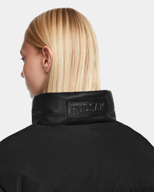 A person with straight blonde hair is shown from behind, wearing the Rudsak OPRAH - 8124708 Black textured women’s cropped down puffer jacket with a raised collar featuring a black Rudsak label.