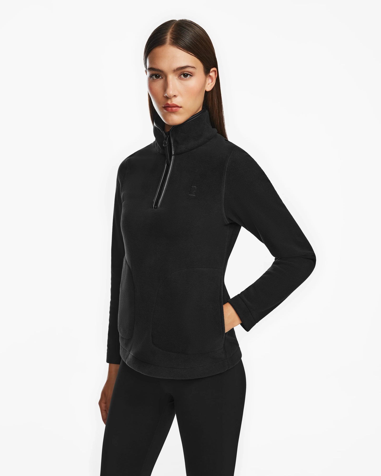 A woman with straight brown hair wears Rudsaks ORCHID - 8524616 Black womens fitted half-zip pullover sweater and black leggings, standing against a white background with one hand on her hip.