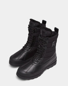The Rudsak REAGAN - 6224501 Black boots feature a lace-up design, thick rubber soles, and faux fur lining—ideal men’s winter boots for warmth and style, shown against a plain white background.