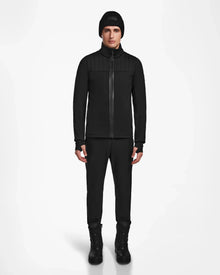 A person stands facing forward, wearing the Rudsak TREVOR - 6124519 Black mens ski jacket, black pants, and black lace-up boots against a plain white background.
