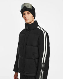 A man in a black Rudsak USHER - 6124516 down ski jacket with white sleeve stripes, a black knit beanie, and ski goggles on his forehead stands against a plain white background.