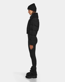 A person in profile against a white background models winter fashion, featuring the Rudsak YVETTE - 8124710 Black womens crop down puffer jacket, paired with a black beanie, black leggings, and black boots.