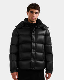 A man with short dark hair models the Rudsak BRAYDEN S - M125525 Black water-resistant quilted down puffer jacket with a high collar, standing against a plain light gray background.