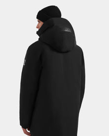 A person is shown from the back and slightly to the side, wearing the Rudsak COREY - M125512 Black men’s down parka with a black knit beanie, against a plain light gray background.